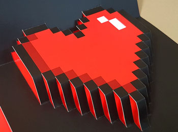 Una tarjeta de felicitación pop up para el Día de San Valentín que tiene un diseño de un corazón troquelado a modo de pixel